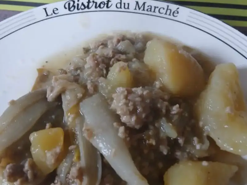 Plate of braised Belgian endive with ground meat and potatoes, stainless steel pot in the background