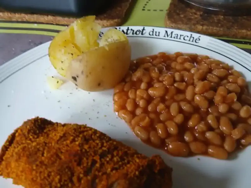 Crispy paprika-breaded meat patty, white beans in tomato sauce and a jacket potato on a plate