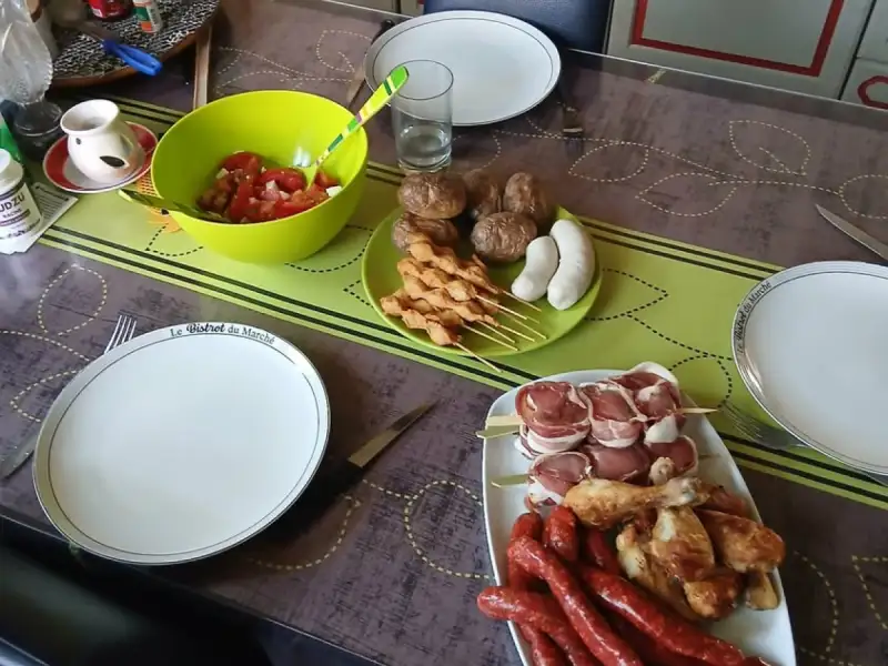 Raw chicken kebabs on a cookout table with sausages, drumsticks, bacon rolls and tomato salad