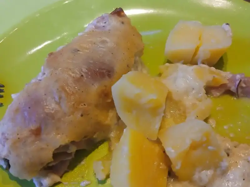 Golden baked prosciutto-wrapped chicken roll-ups with creamy potatoes on a green plate