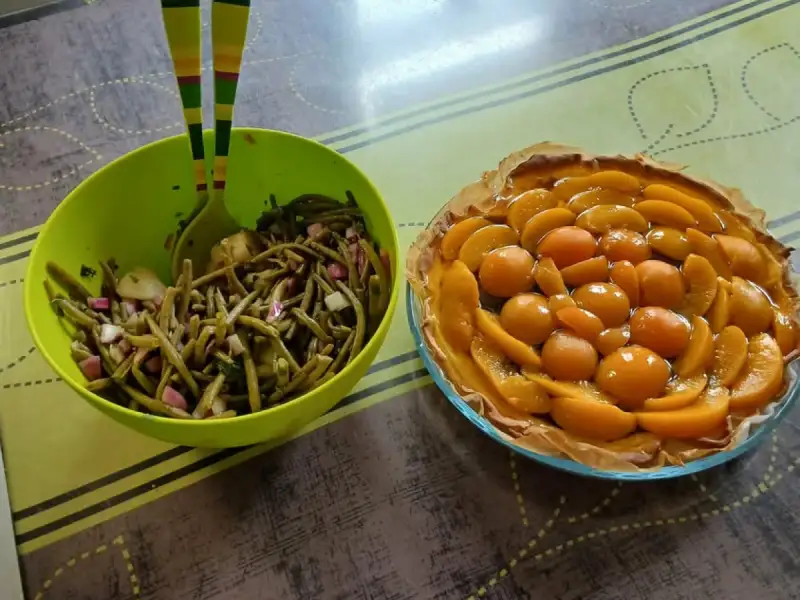 Green bean salad with red onion and cucumber in a green salad bowl, next to a peach tart