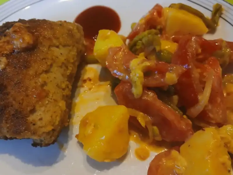Golden slice of meatloaf with pan-fried potatoes, tomatoes and green beans on a plate