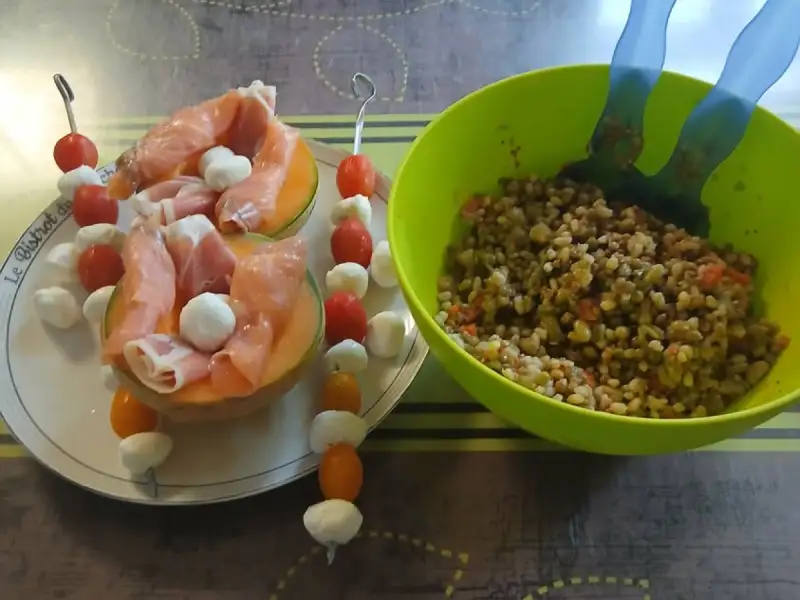 Melon halves filled with prosciutto and mozzarella pearls, cherry tomato and mozzarella skewers, next to a bowl of salad