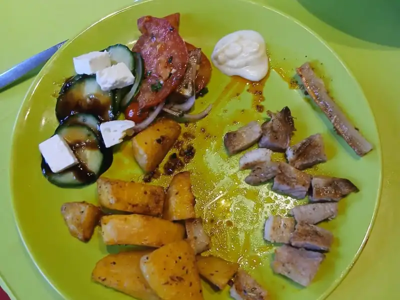 Plate of seared pork chop pieces, roasted potatoes and Greek salad with cucumber, tomatoes and feta